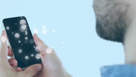 Animation-of-multiple-white-spots-over-man-using-smartphone-on-blue-background