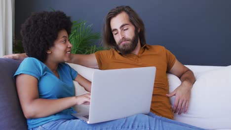 Mixed-race-couple-sitting-on-sofa-using-laptop-in-living-room