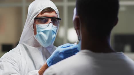 Caucasian-male-medical-worker-wearing-protective-clothing-taking-dna-swab-sample-from-patient-in-lab