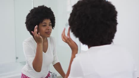Afroamerikanische-Frau-Berührt-Ihr-Gesicht,-Während-Sie-Im-Badezimmer-In-Den-Spiegel-Schaut