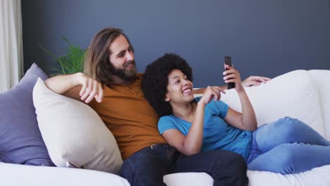 Gemischtes-Rassenpaar,-Das-Zu-Hause-Auf-Dem-Sofa-Einen-Videoanruf-Auf-Dem-Smartphone-Führt