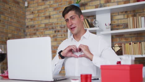 Caucasian-man-making-video-call-using-laptop-making-love-heart-shape-and-talking
