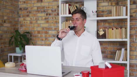 Caucasian-man-making-video-call-using-laptop-drinking-glass-of-wine-and-talking