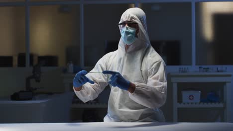 Caucasian-male-medical-worker-wearing-protective-clothing-and-gloves-using-handheld-interface-in-lab