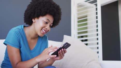 Afroamerikanische-Frau-Benutzt-Smartphone,-Während-Sie-Zu-Hause-Auf-Der-Couch-Sitzt