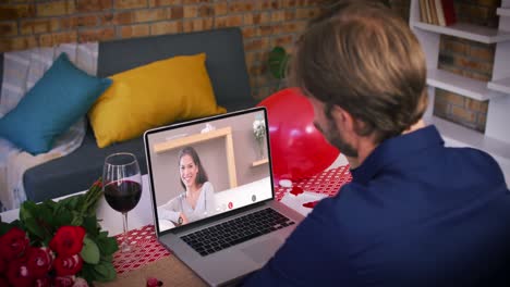 Caucasian-couple-on-a-valentines-date-video-call-man-waving-to-smiling-woman-on-laptop-screen