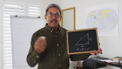 Mixed-race-male-teacher-standing-at-a-whiteboard-giving-an-online-lesson-to-camera