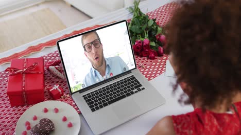 Diverse-couple-on-a-valentines-date-video-call-woman-blowing-kiss-to-man-on-laptop-screen
