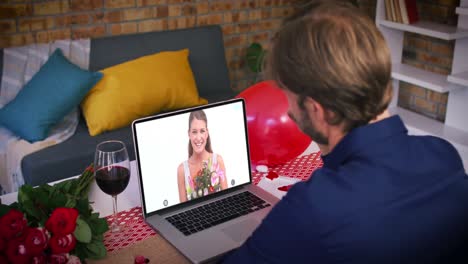 Kaukasisches-Paar-Bei-Einem-Valentinstag-Videoanruf,-Lächelnde-Frau-Auf-Dem-Laptop-Bildschirm,-Die-Blumen-Hält