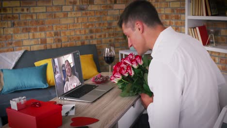 Diverse-couple-making-valentines-date-video-call-man-holding-flowers-woman-laughing-on-laptop-screen