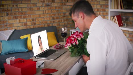 Kaukasisches-Paar-Bei-Einem-Valentinstag-Videoanruf,-Frau-Auf-Laptop-Bildschirm,-Lächelnder-Mann-Mit-Blumen