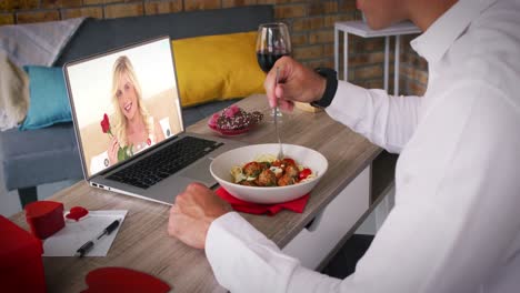 Kaukasisches-Paar-Bei-Einem-Valentinstag-Videoanruf,-Frau-Auf-Laptop-Bildschirm,-Lächelnder-Mann-Beim-Essen