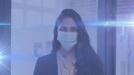 Blue-light-trails-against-portrait-of-indian-woman-wearing-facemask-at-office