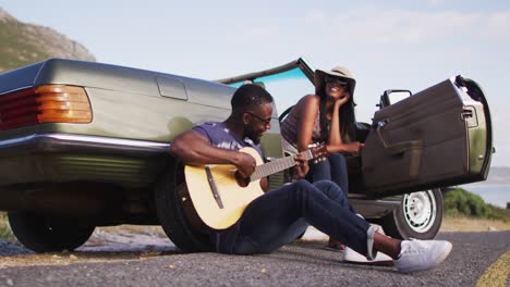 Hombre-Afroamericano-Tocando-La-Guitarra-Para-Su-Novia-Mientras-Está-Sentado-En-La-Carretera
