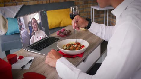 Caucasian-couple-on-a-valentines-date-video-call-woman-on-laptop-screen-laughing-man-eating-meal