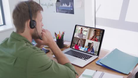 Caucasian-man-using-laptop-and-phone-headset-on-video-call-with-colleagues