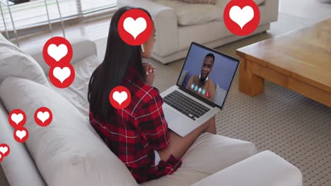 Animation-Von-Social-Media-Herzsymbolen-über-Einer-Frau,-Die-Im-Hintergrund-Einen-Laptop-Mit-Videoanruf-Verwendet