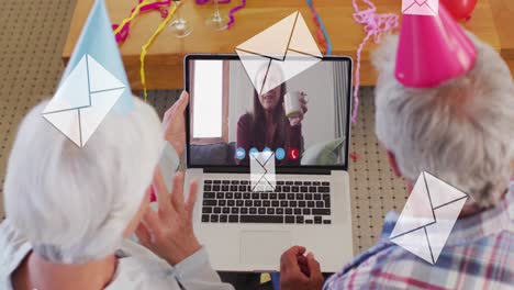 Animation-of-mail-envelopes-over-senior-couple-wearing-party-hats-using-laptop-on-video-call-in-back