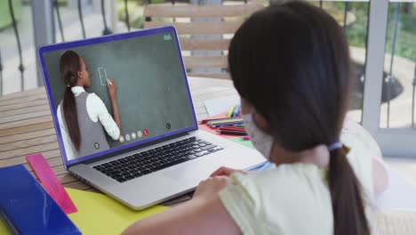 Kaukasisches-Schulmädchen-Mit-Gesichtsmaske,-Das-Einen-Laptop-Bei-Einem-Videoanruf-Mit-Einer-Lehrerin-Benutzt