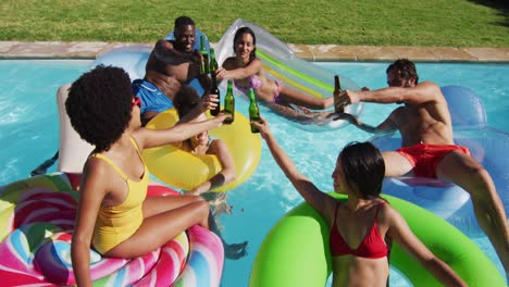 Diverse-group-of-friends-having-fun-playing-on-inflatables-making-a-toast-in-swimming-pool