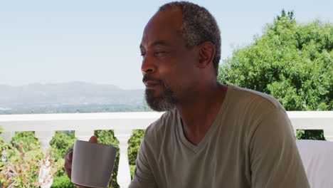 Älterer-Afroamerikanischer-Mann-Trinkt-Kaffee,-Während-Er-Zu-Hause-Auf-Dem-Balkon-Sitzt