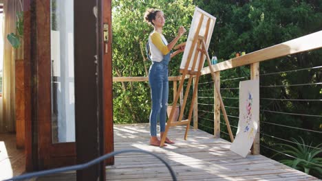 Mixed-race-woman-painting-on-canvas-in-the-balcony-at-home