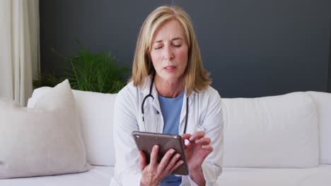 Portrait-of-caucasian-senior-female-doctor-using-digital-tablet-while-having-a-video-call-at-home