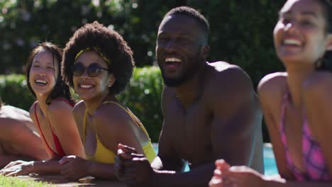 Diverse-group-of-friends-standing-at-the-poolside-talking-and-looking-at-the-camera