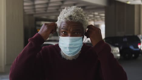Portrait-of-african-american-senior-man-wearing-face-mask-in-the-parking-lot