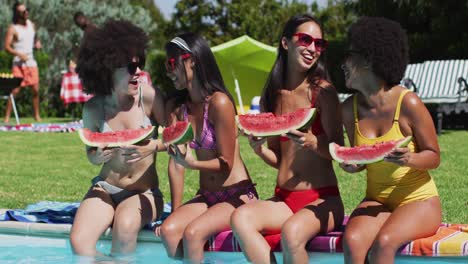 Gruppe-Verschiedener-Mädchen,-Die-Wassermelone-In-Der-Hand-Halten-Und-Miteinander-Reden,-Während-Sie-Am-Pool-Sitzen