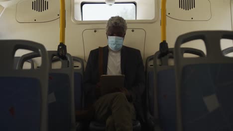 Hombre-Mayor-Afroamericano-Con-Mascarilla-Usando-Tableta-Digital-Mientras-Está-Sentado-En-El-Autobús