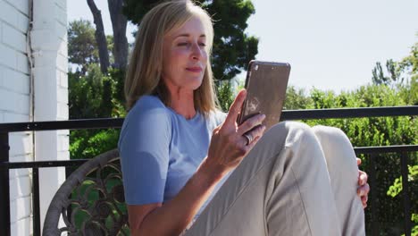 Senior-caucasian-woman-using-tablet-sitting-in-sunny-garden
