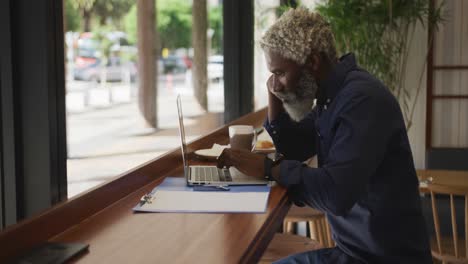 Hombre-Mayor-Afroamericano-Usando-Una-Computadora-Portátil-Mientras-Está-Sentado-En-El-Café