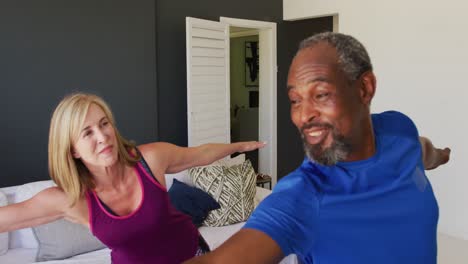 Diverse-senior-couple-exercising-together-at-home-smiling-and-stretching