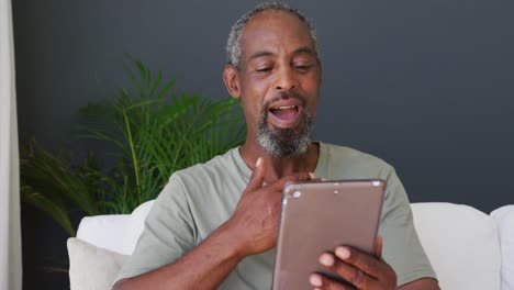 Älterer-Afroamerikanischer-Mann,-Der-Einen-Videoanruf-Auf-Einem-Digitalen-Tablet-Führt,-Während-Er-Zu-Hause-Auf-Der-Couch-Sitzt