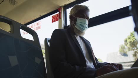 Afroamerikanischer-älterer-Mann-Mit-Gesichtsmaske-Und-Laptop,-Während-Er-Im-Bus-Sitzt