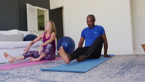 Diverse-senior-couple-exercising-together-at-home-sitting-on-exercise-mats-stretching