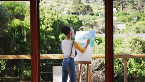 Mixed-race-woman-painting-on-canvas-in-the-balcony-at-home