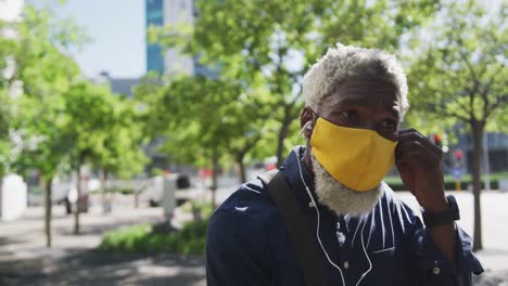 Close-up-of-african-american-senior-man-in-face-mask-wearing-earphones-on-the-road