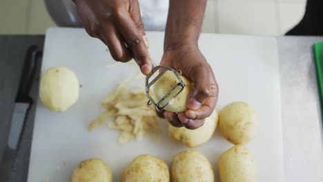 Mittelteil-Einer-Afroamerikanischen-Köchin,-Die-In-Der-Restaurantküche-Kartoffeln-Schält