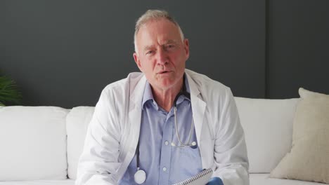 Portrait-of-caucasian-senior-male-doctor-holding-covid-19-vaccine-while-having-a-video-call