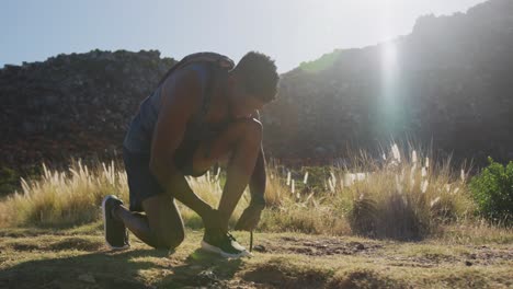 African-american-man-exercising-outdoors-tying-his-shoe-in-countryside-on-a-mountain