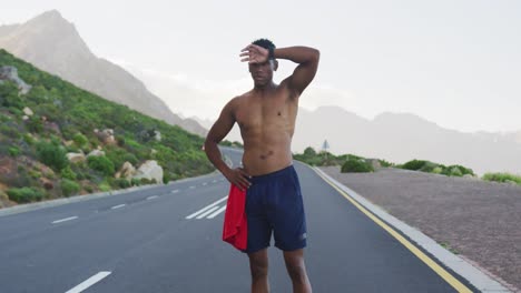Hombre-Afroamericano-De-Pie-Y-Flexionando-Sus-Músculos-En-Una-Carretera-Costera