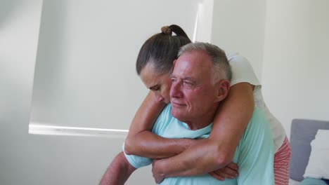 Caucasian-senior-woman-hugging-her-husband-from-behind-at-home