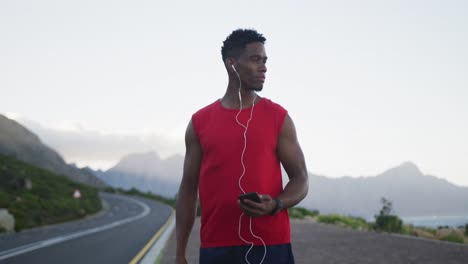 Hombre-Afroamericano-Con-Auriculares-Sosteniendo-Un-Teléfono-Inteligente-En-La-Carretera