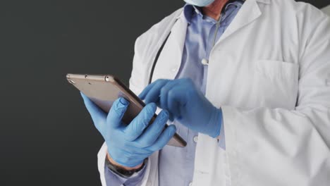 Mid-section-of-caucasian-male-doctor-wearing-surgical-gloves-using-digital-tablet