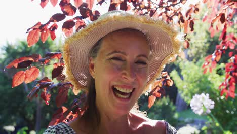 Retrato-De-Una-Mujer-Mayor-Caucásica-Feliz-En-El-Jardín-Usando-Sombrero-Para-El-Sol-Y-Sonriendo-Bajo-El-Sol