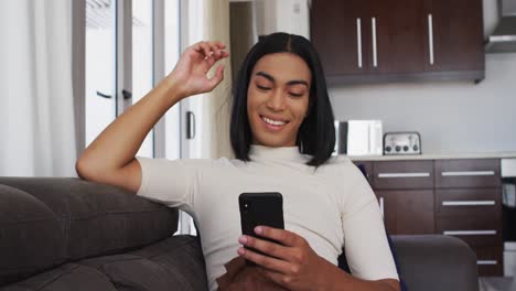 Gender-fluid-male-smiling-while-using-smartphone-sitting-on-the-couch-at-home