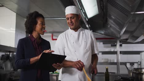African-american-female-manager-holding-clipboard-and-talking-with-chef
