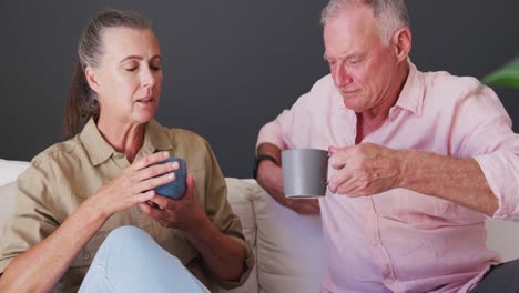Caucasian-senior-couple-holding-coffee-cup-talking-to-each-other-while-sitting-on-the-couch-at-home